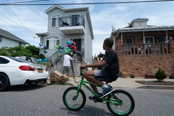 A boy bicycles by a memorial for ten-year-old Justin Wallace outside the Far Rockaway home where he was shot and killed. The brick house next door is where the Lochans live and where police found several illegal weapons during a search warrant.